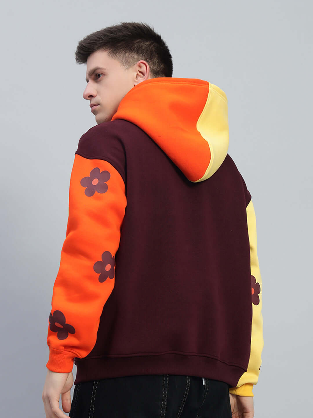 Back view of Cosmos Oversized Fleece Hoodie in vibrant multi-color design with floral patterns on sleeves, featuring orange and yellow tones.