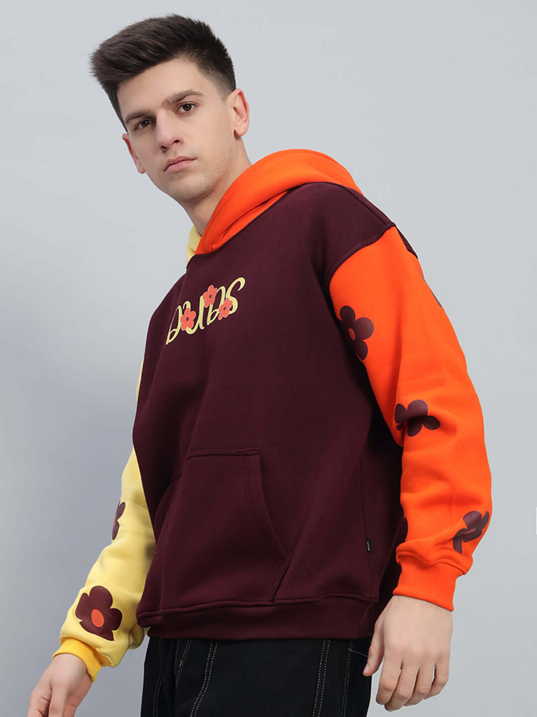 Model wearing COSMOS Oversized Fleece Hoodie in multi-color with bold floral accents, featuring maroon, orange, and yellow hues.