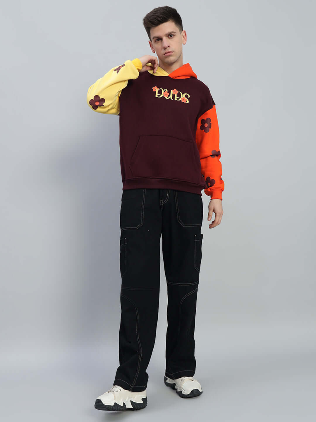 Model wearing COSMOS Oversized Fleece Hoodie Multi with colorful floral pattern and black pants, showcasing modern streetwear style.