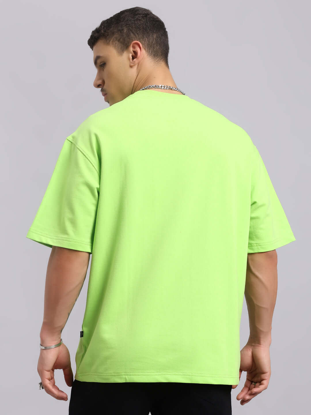 Model wearing ORCAS oversized neon green t-shirt in premium heavy gauge fabric, showcasing back view.