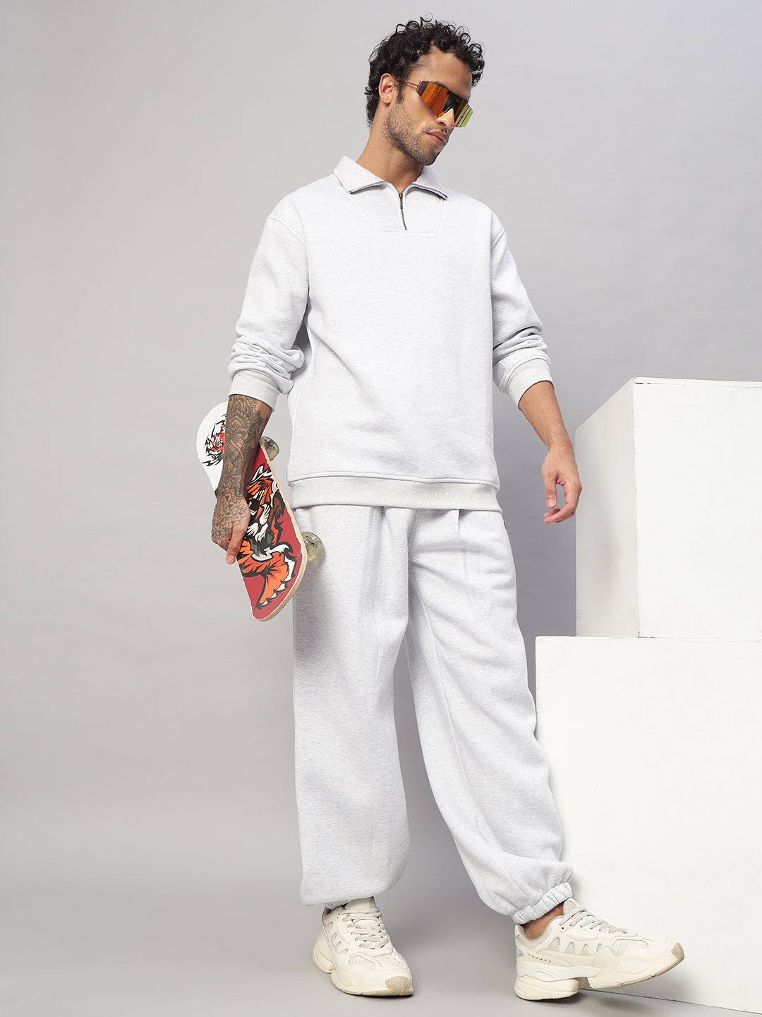Model wearing BONA-FIDE FLEECE CO-ORD MELANGE GREY, holding a skateboard, showcasing casual style in a grey outfit with sunglasses.