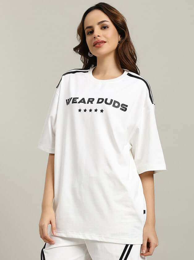 Model wearing women's star jumper oversized t-shirt in off white, featuring a 'Wear Duds' logo and stars, styled with casual pants.