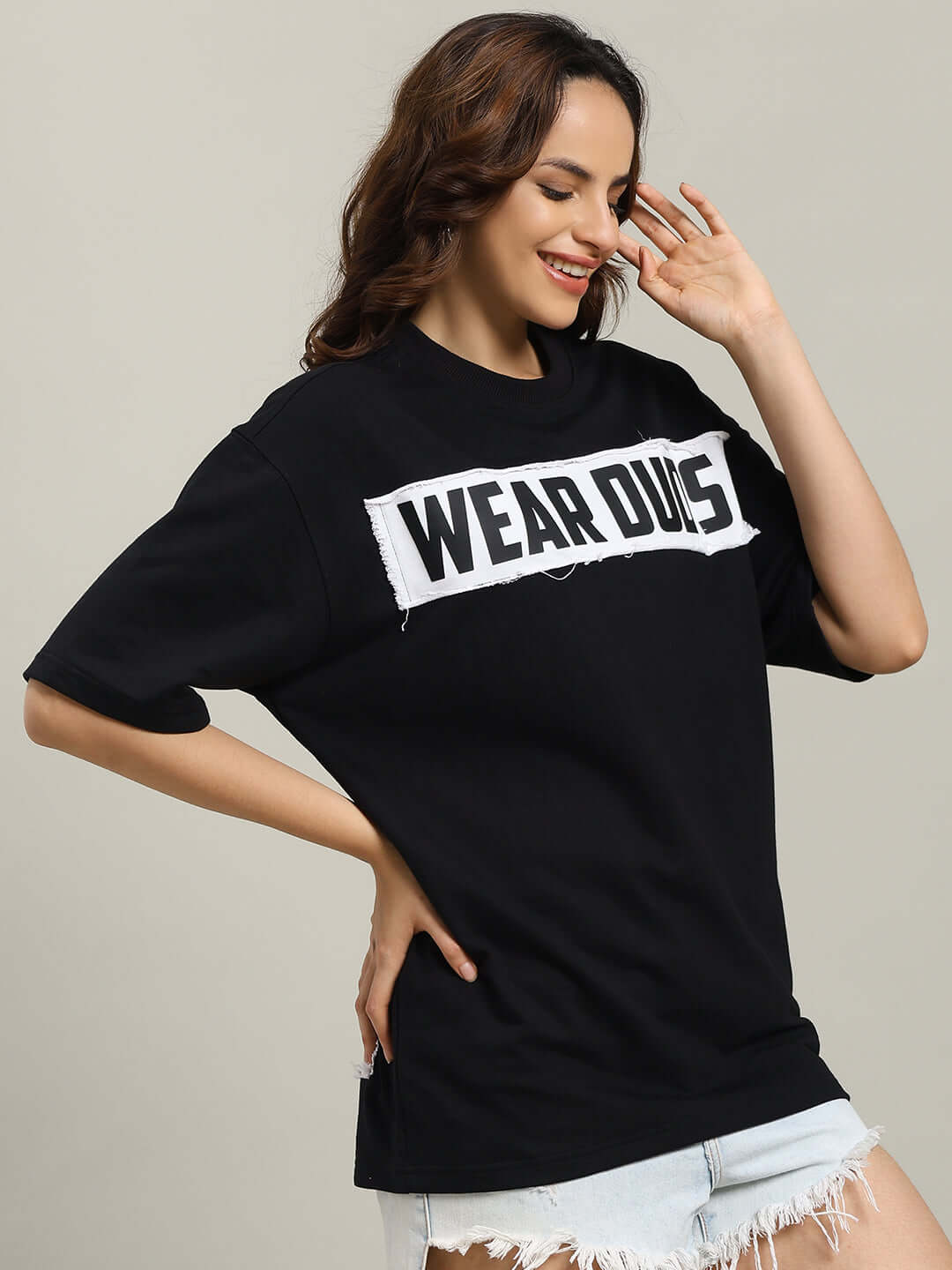 Woman wearing a black oversized Harley designer T-shirt with 'WEAR DUES' text, made from premium cotton fabric, styled with denim shorts.