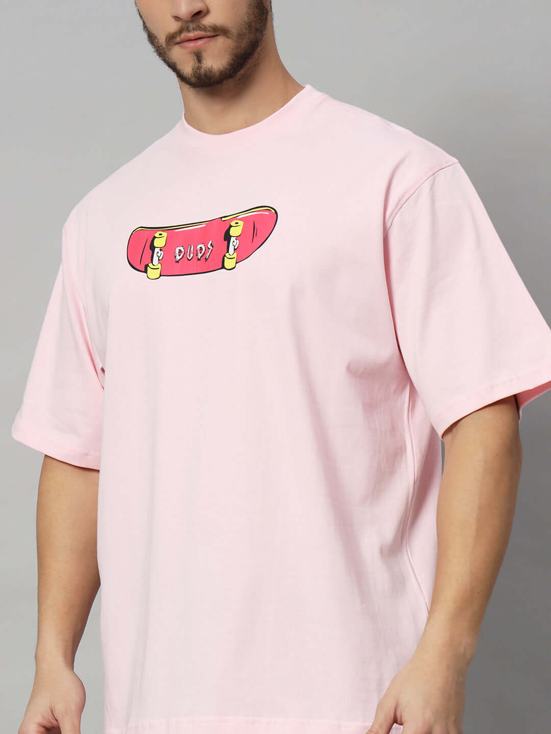 Man wearing ROWDY APE OVER-SIZED T-SHIRT PINK with skateboard design, customizable size available.