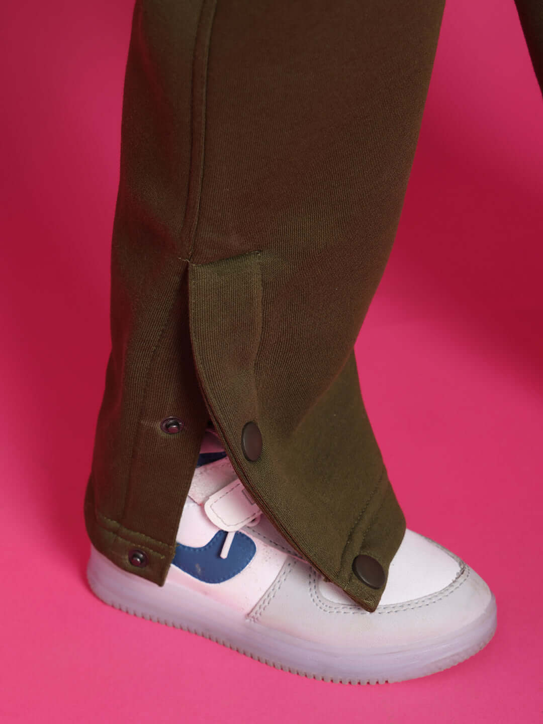 Olive green co-ord pant detail with buttons on pink background, styled with white sneaker for boys and girls.