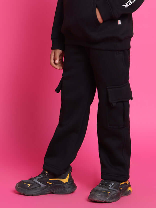 Child wearing black Monster Co-Ord set with cargo pockets, standing against a pink background.