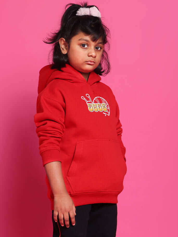 Child wearing red hoodie and black pants from Snail Co-ord collection, standing against a pink background.