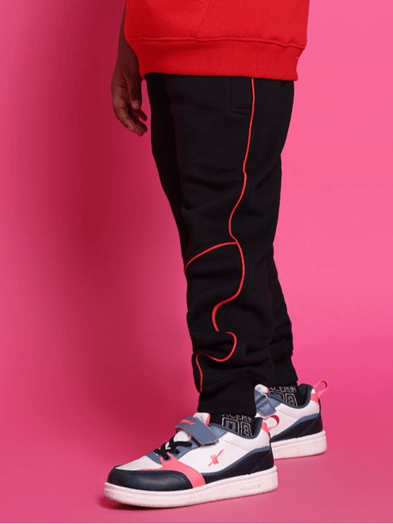 Child wearing SNAIL red-black co-ord outfit with trendy sneakers against a pink background.