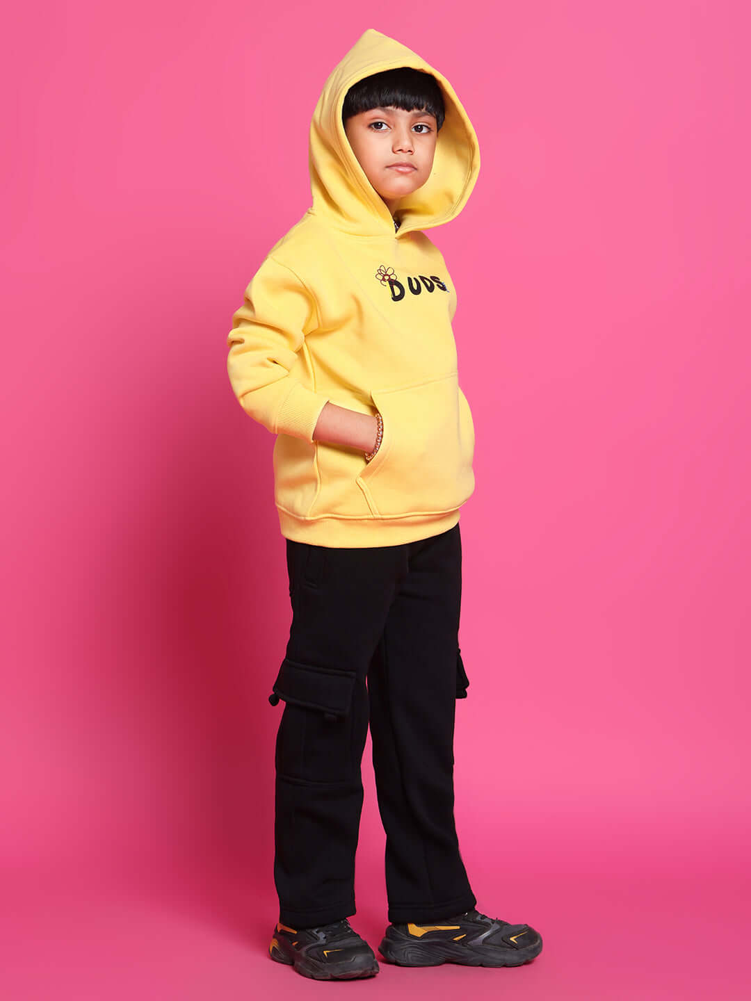 Kid wearing yellow Cool Dude hoodie and black pants, standing against pink background, showcasing trendy co-ord outfit for boys and girls.