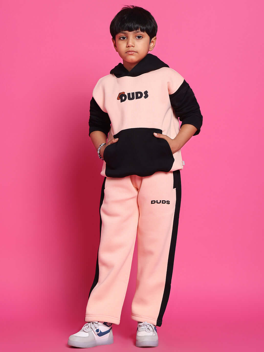 Child wearing black-beige Club House fleece jogger, standing against pink background; cozy and stylish kids' fashion.