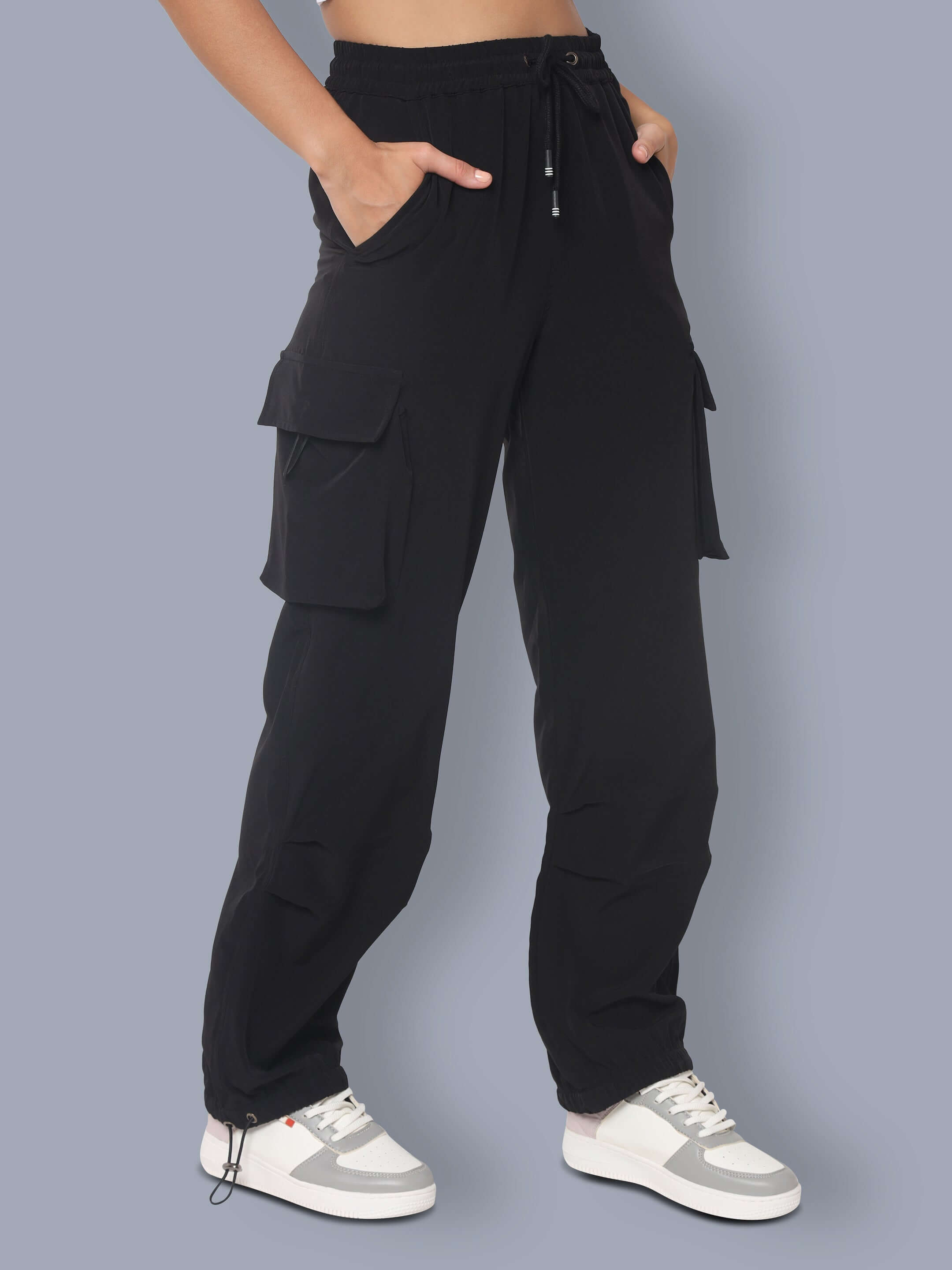 Woman wearing black tactical cargo joggers with pockets and drawstring waist, styled with casual sneakers.