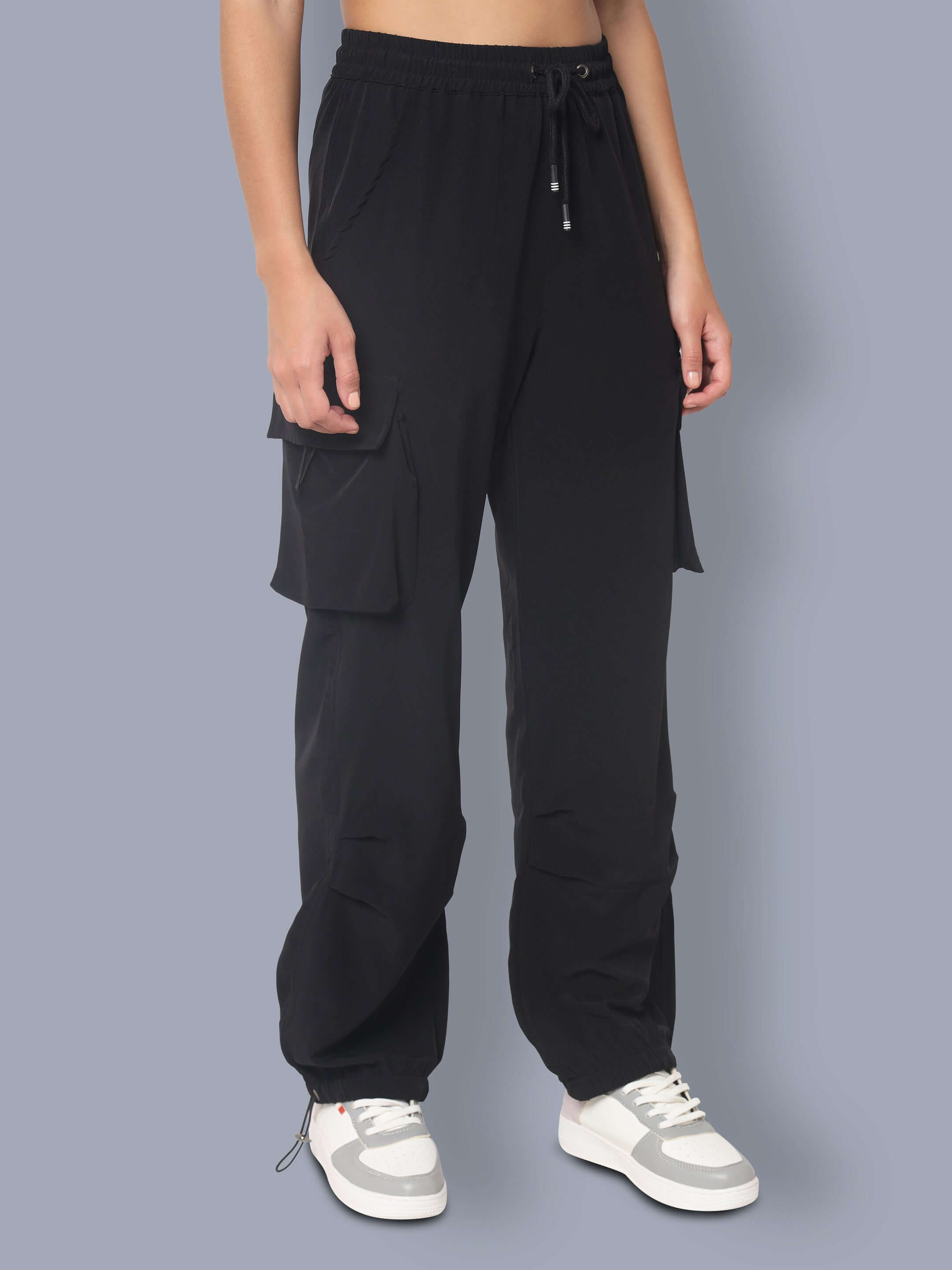 Black women's tactical cargo joggers with large pockets and drawstring waist, displayed with white sneakers on a gray background.