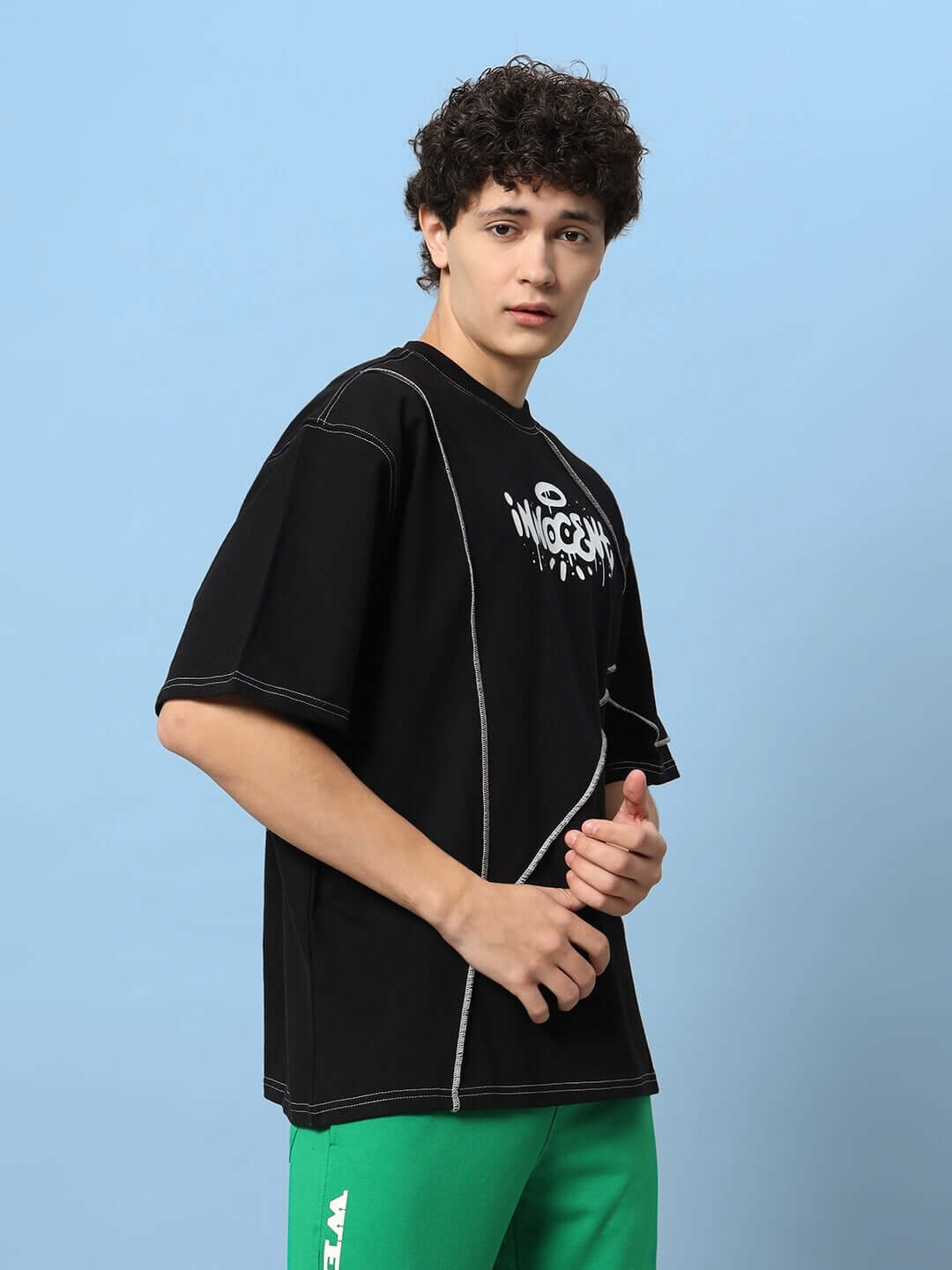 Model wearing INNOCENT CONTRAST STITCHED OVER-SIZED T-SHIRT BLACK with premium cotton French terry fabric against a blue background