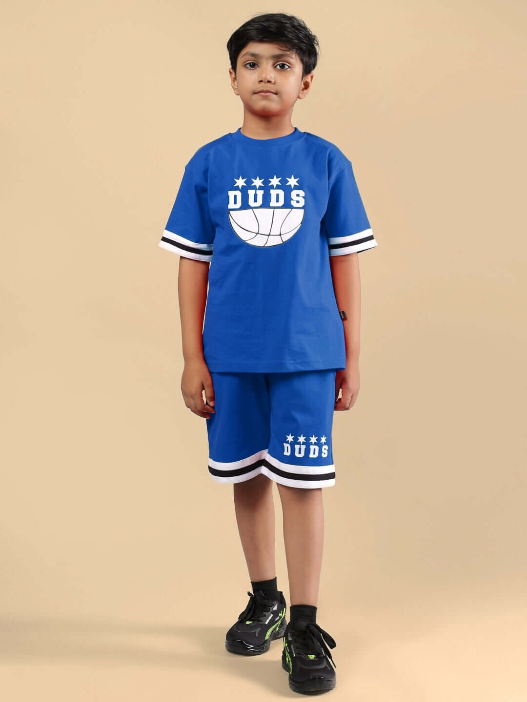 Young model wearing vibrant blue DIGGIN shorts and shirt set for boys and girls, showcasing style and comfort from DUDS brand.