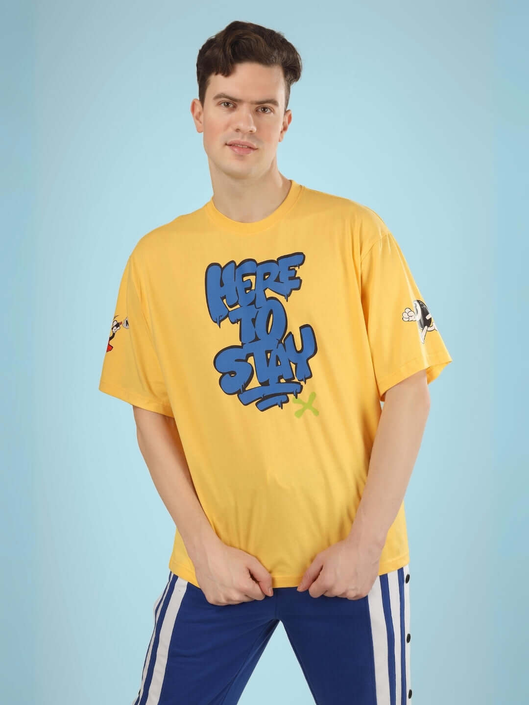 Model wearing HERE TO STAY OVER-SIZED T-SHIRT YELLOW with bold graphic, vibrant street style, premium cotton.