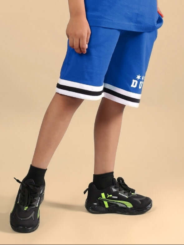 Child wearing blue DIGGIN shorts for boys & girls, showcasing sporty design with white stripes and black sneakers.