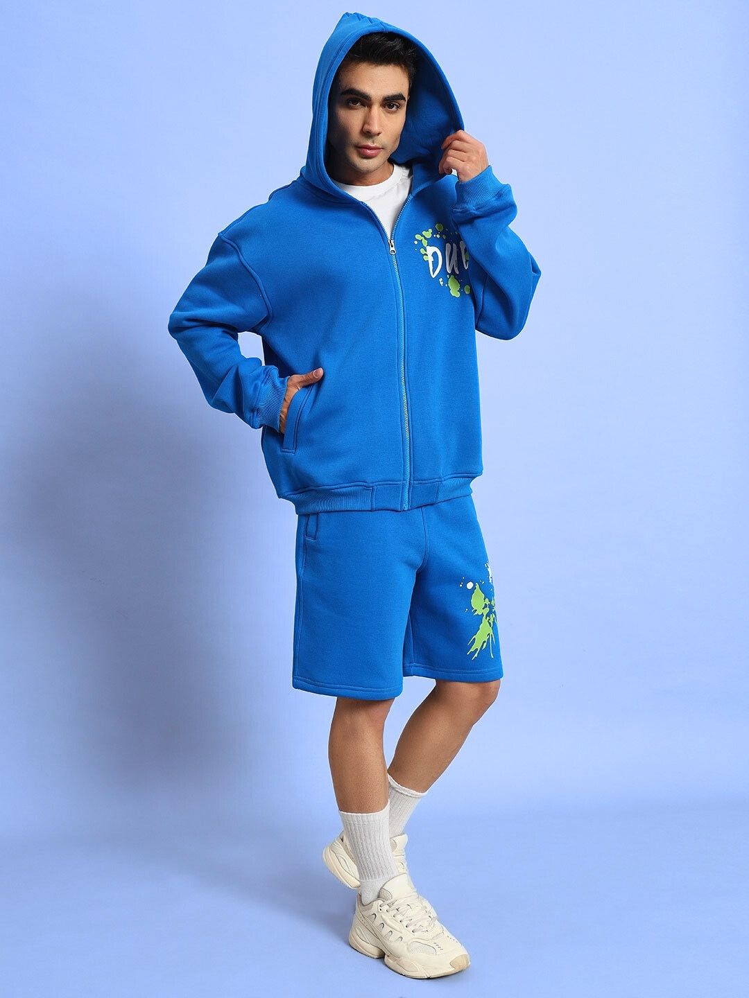 Man wearing a royal blue fleece co-ord with hoodie and shorts, branded 'No Drama', standing against a blue background.