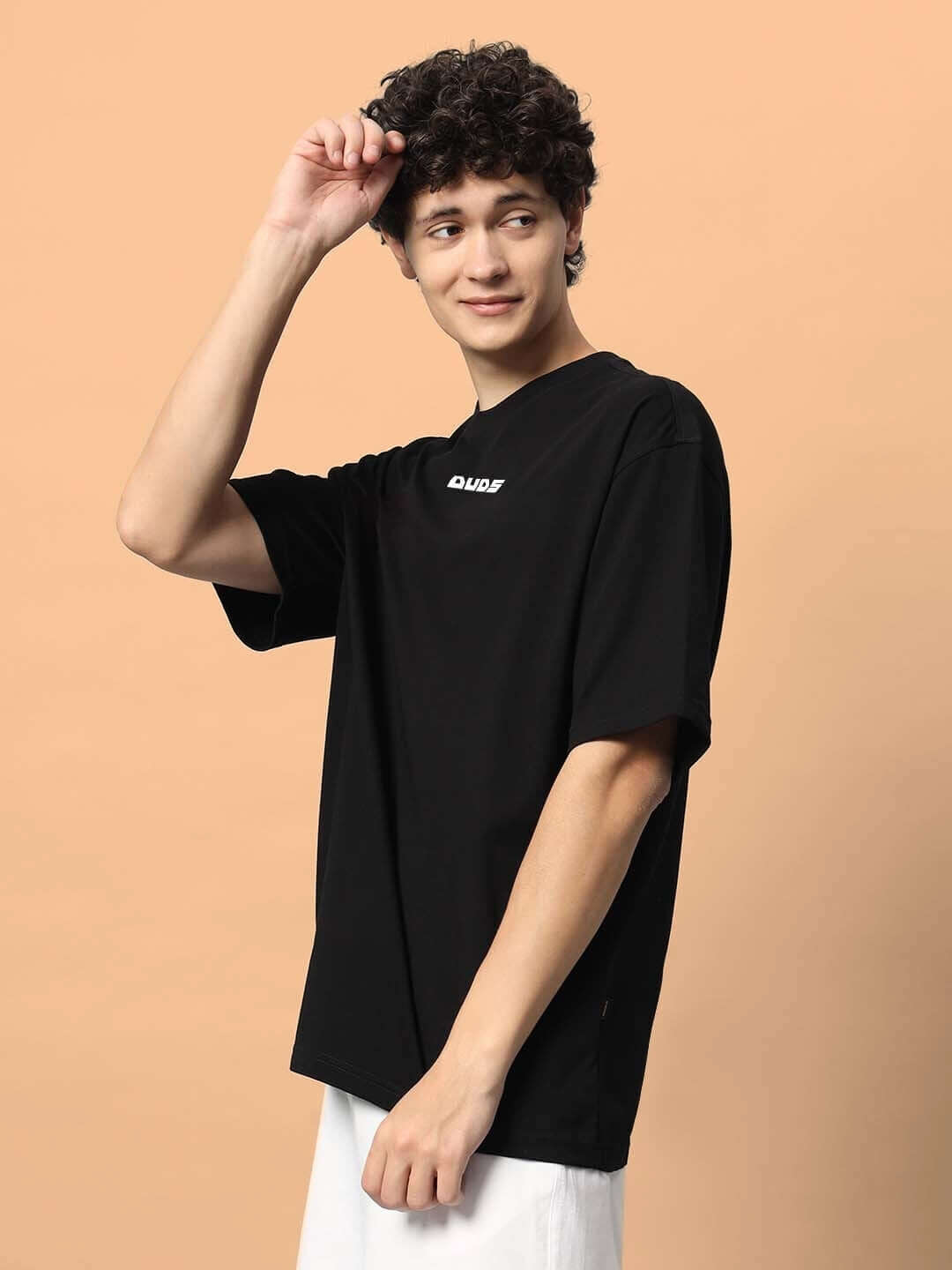 Man wearing TOO LOUD OVER-SIZED T-SHIRT BLACK against a beige background.