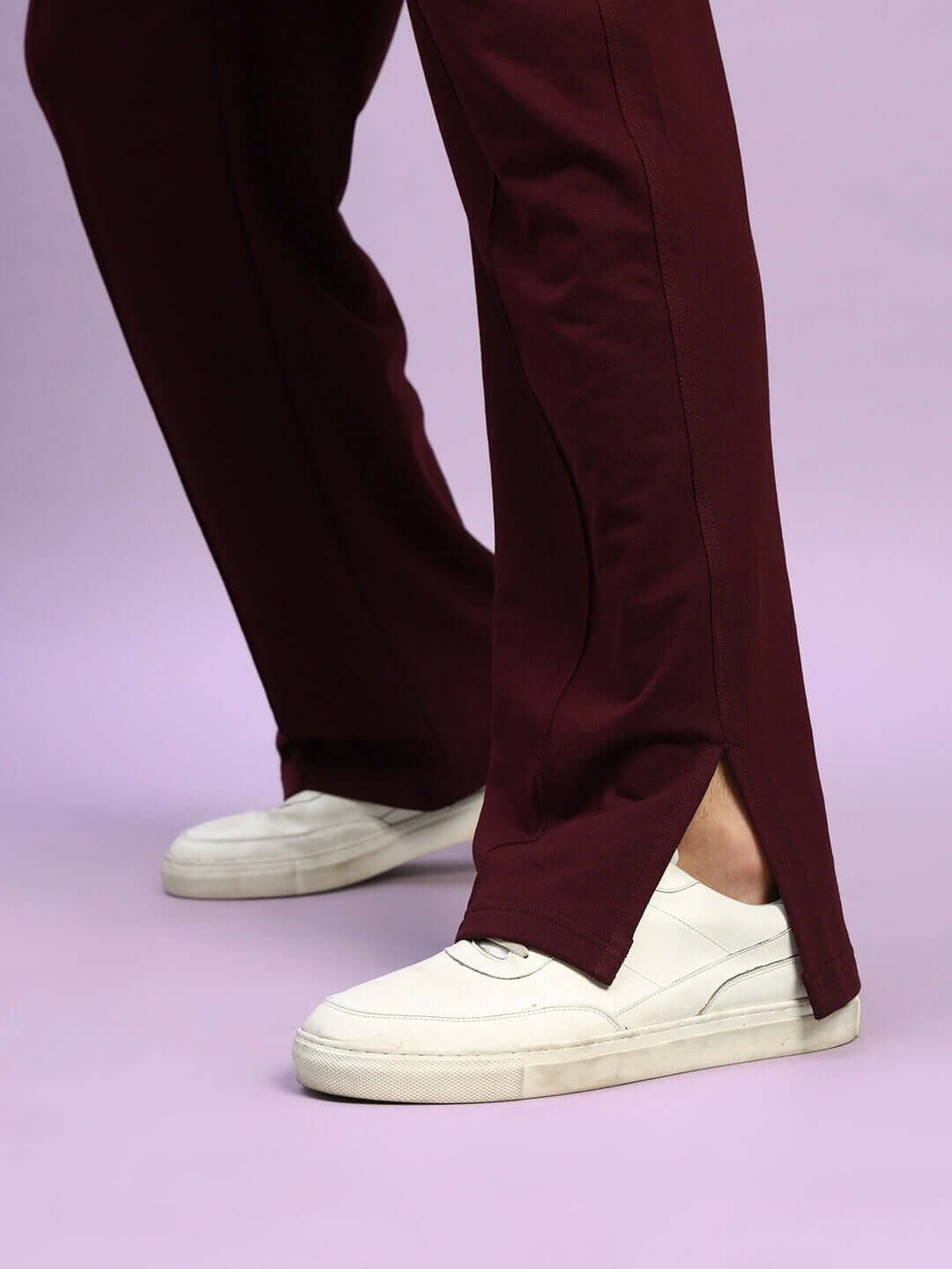 Close-up of ZION maroon joggers with a relaxed fit, featuring an elasticated waistband and side slit, paired with white sneakers.