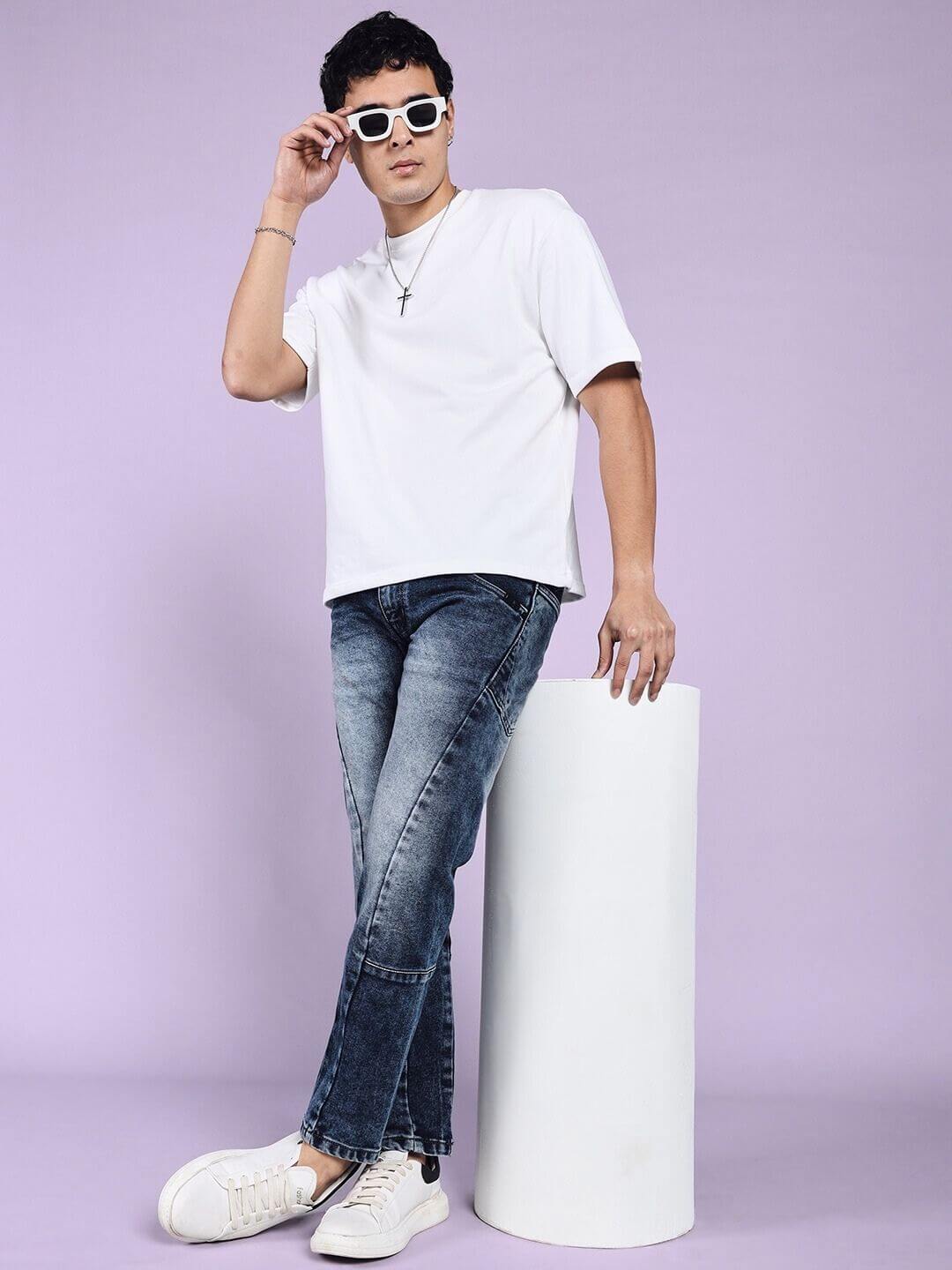 Man wearing LAPIS faded regular fit denim jeans in blue, paired with a white t-shirt and sunglasses, standing against a purple background.