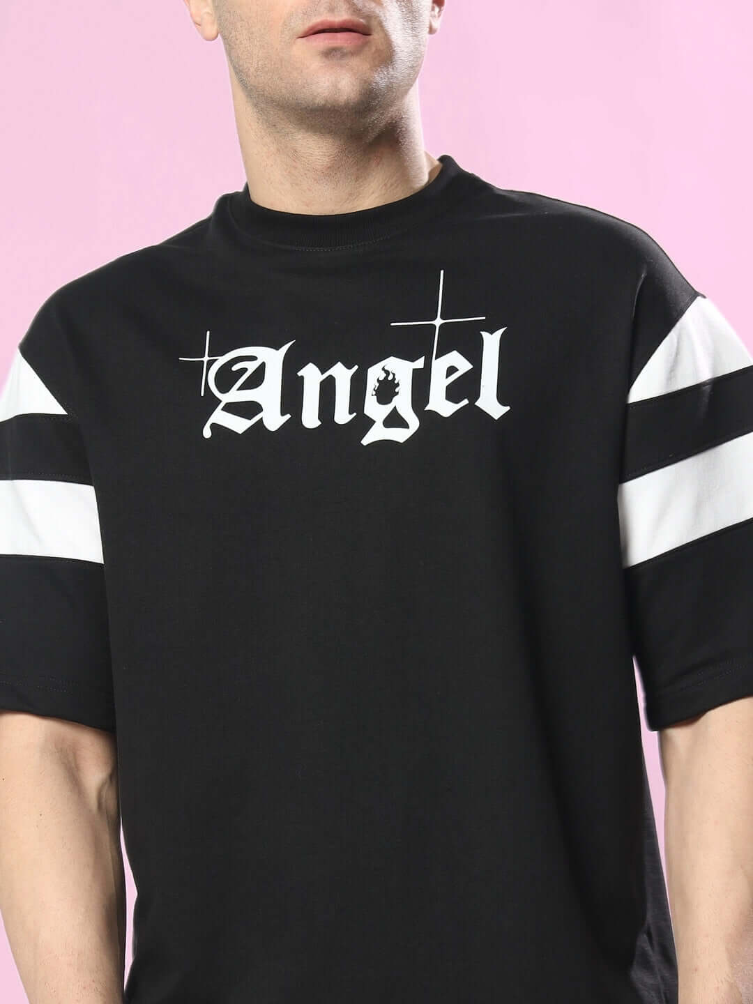 Person wearing DIVINE SPIRIT OVERSIZED T-SHIRT BLACK with 'Angel' text on front, premium cotton blend, against pink background.