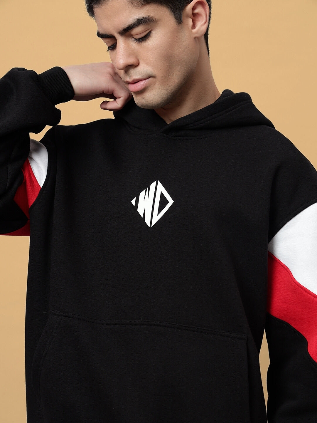 Alt Tag: Black colorblock fleece hoodie from BRIO with red and white accents, worn by a model against a beige background.
