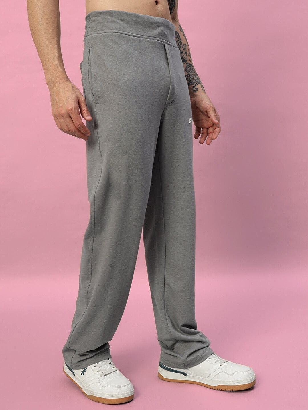 Model wearing NEW ERA Relaxed Fit Joggers in grey, made-to-order with customizable fit option, showcased against a pink background.