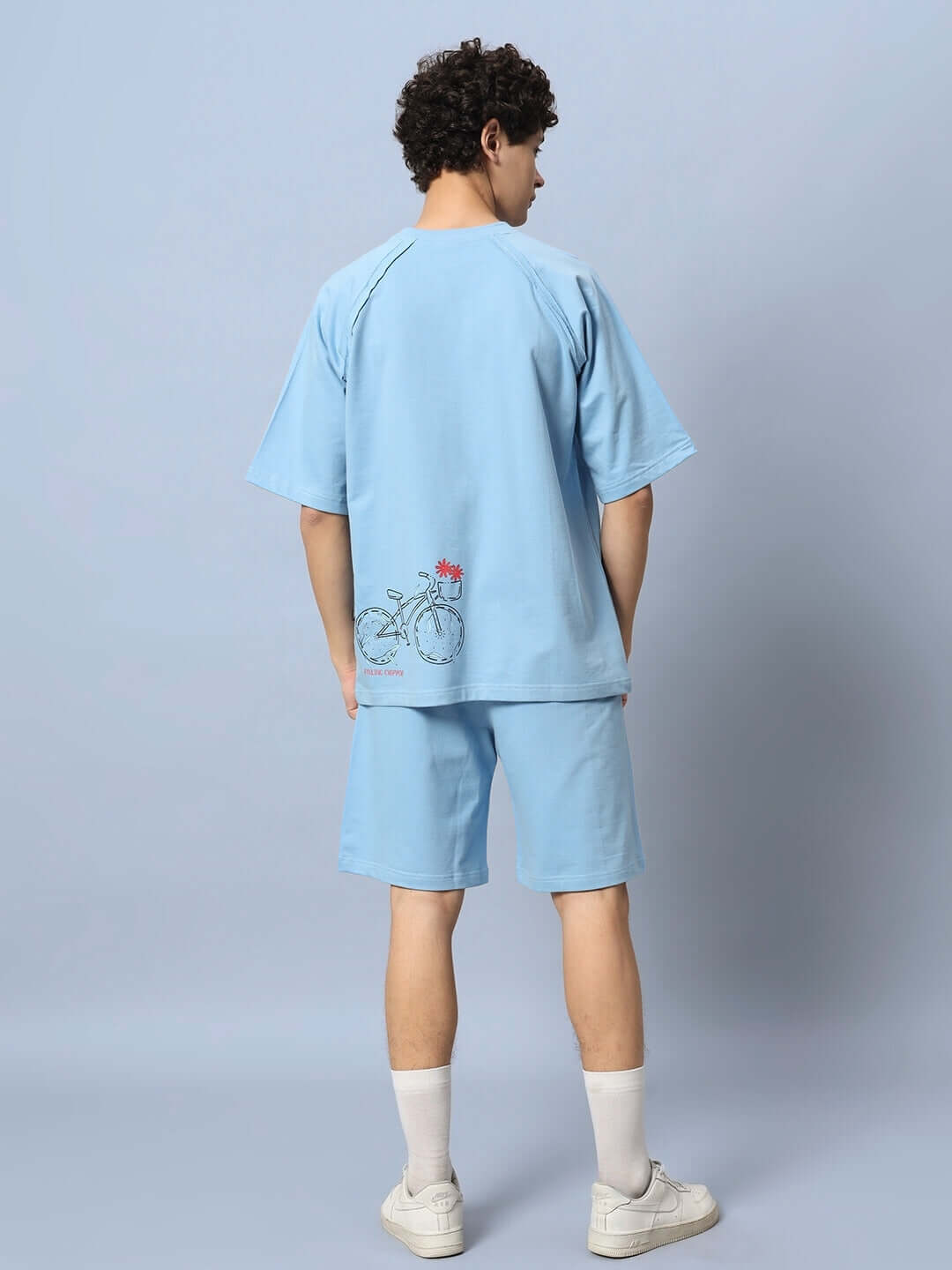Man wearing ENJOY THE RIDE PRINTED CO-ORD SET BLUE with bicycle graphic, premium cotton fabric, rear view against light blue background