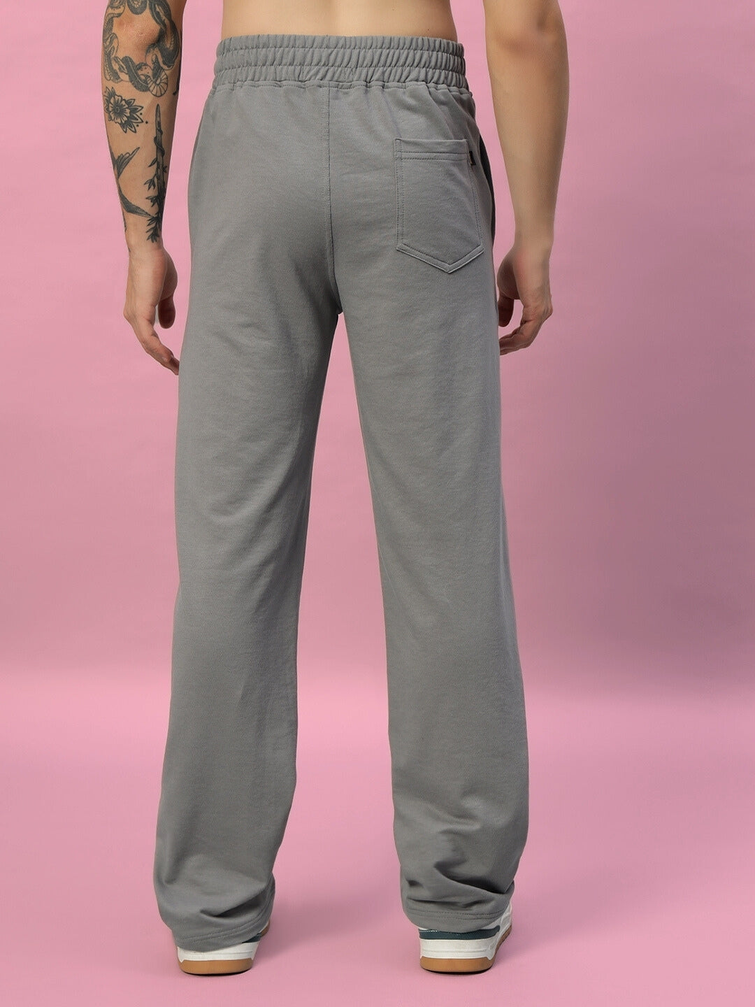 Man wearing New Era Relaxed Fit Joggers in grey, showcasing the rear design against a pink background.