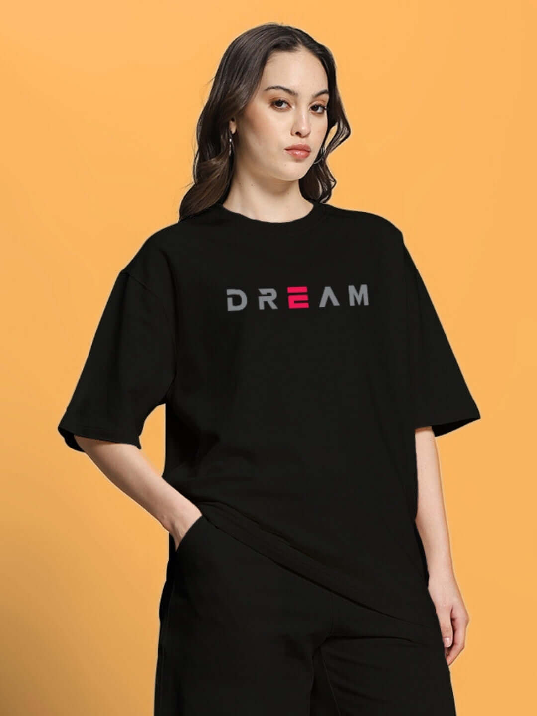Model wearing a women's oversized black T-shirt with 'DREAM' print, made from premium cotton and elastane, by Color By Colours.