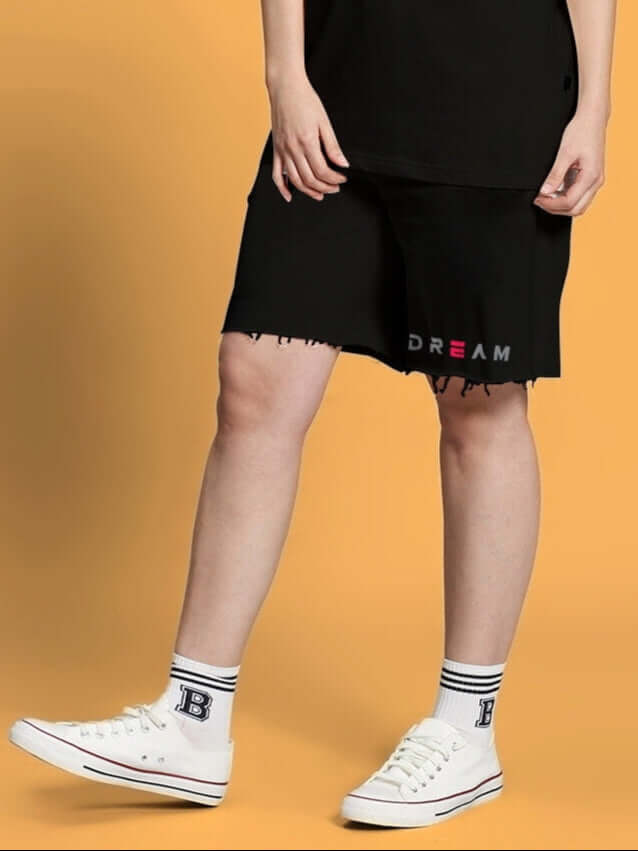 Woman wearing black Women's Fancy Dream Regular Fit Shorts, showcasing casual style with white sneakers on a yellow background.