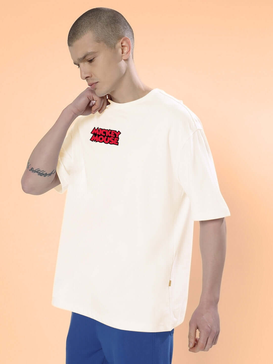 Model wearing DUDS MOUSE OVER-SIZED T-SHIRT OFF WHITE with cartoon logo against peach background.