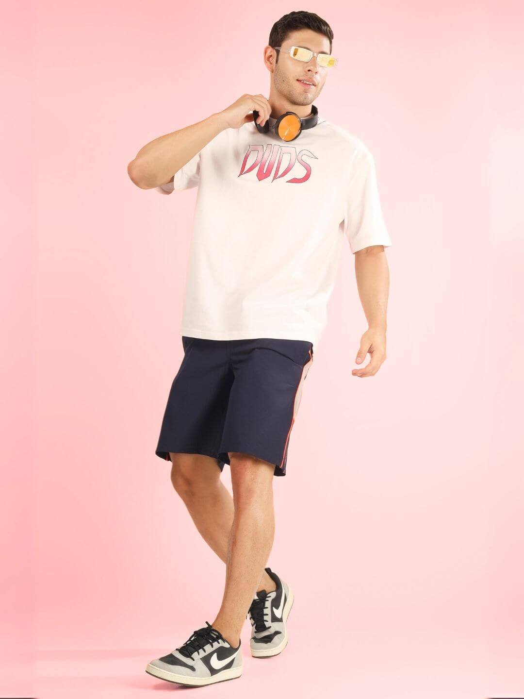 Model wearing CRUEL OVER-SIZED T-SHIRT BABY PINK with sunglasses and headphones, showcasing summer casual style on pink background.
