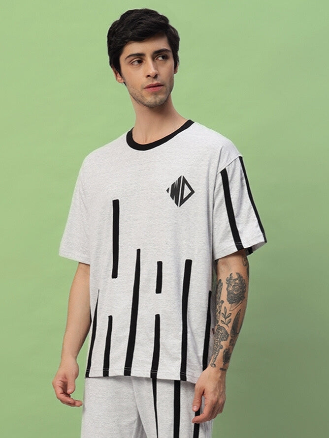Man wearing a melange grey oversized T-shirt with black stripes and graphic design, standing against a green background.