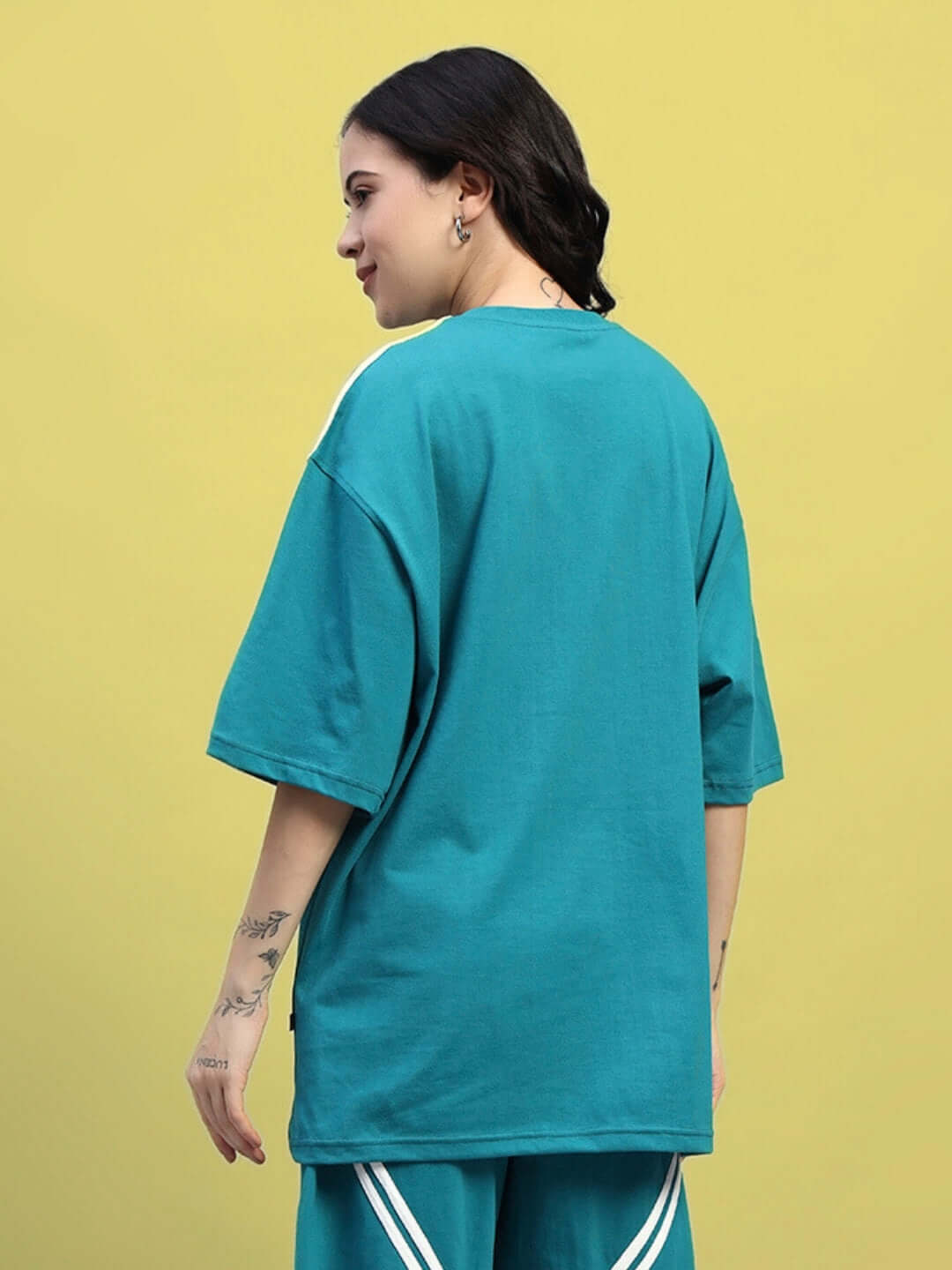 Woman wearing an oversized teal T-shirt made from premium cotton French terry, showcasing casual style against a yellow background.