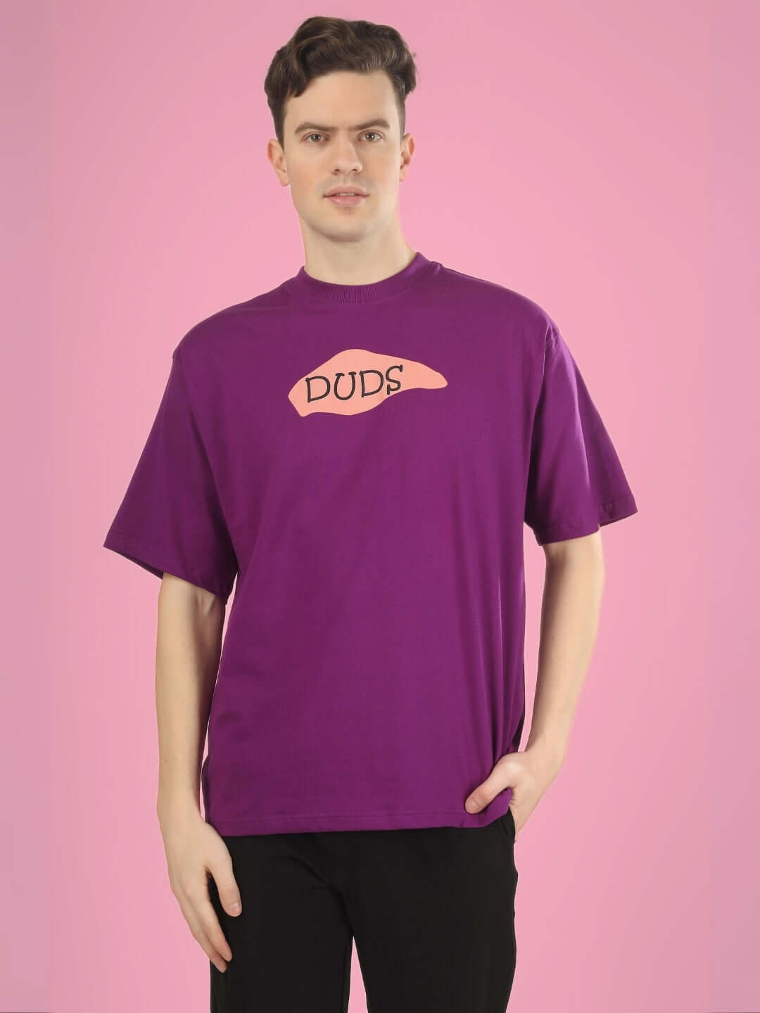 Man wearing WHAT WOW OVER-SIZED PRINTED T-SHIRT PURPLE by DUDS with pink background.