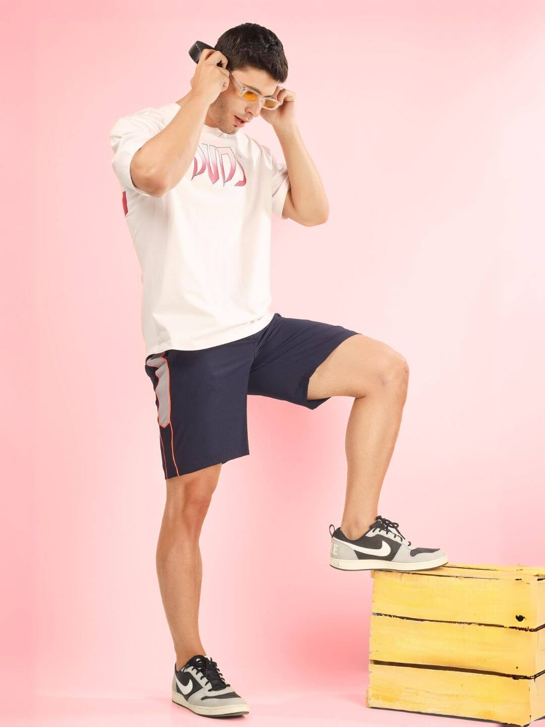 Model wearing CRUEL OVER-SIZED T-SHIRT BABY PINK with navy shorts, posing against a pink background, showcasing fashion style.