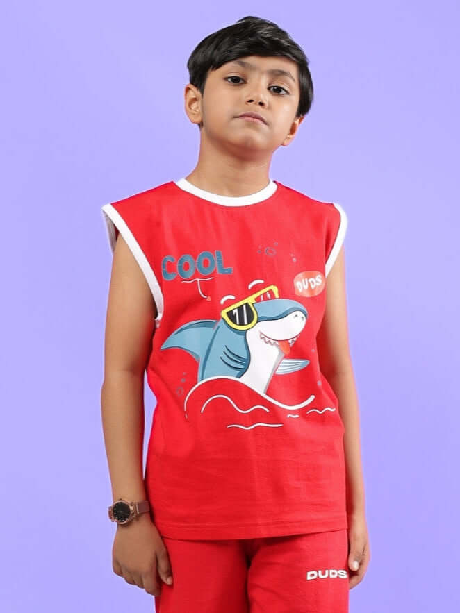 Boy wearing a red Shortfin t-shirt for boys and girls with a playful shark design, made by DUDS, standing against a purple background.