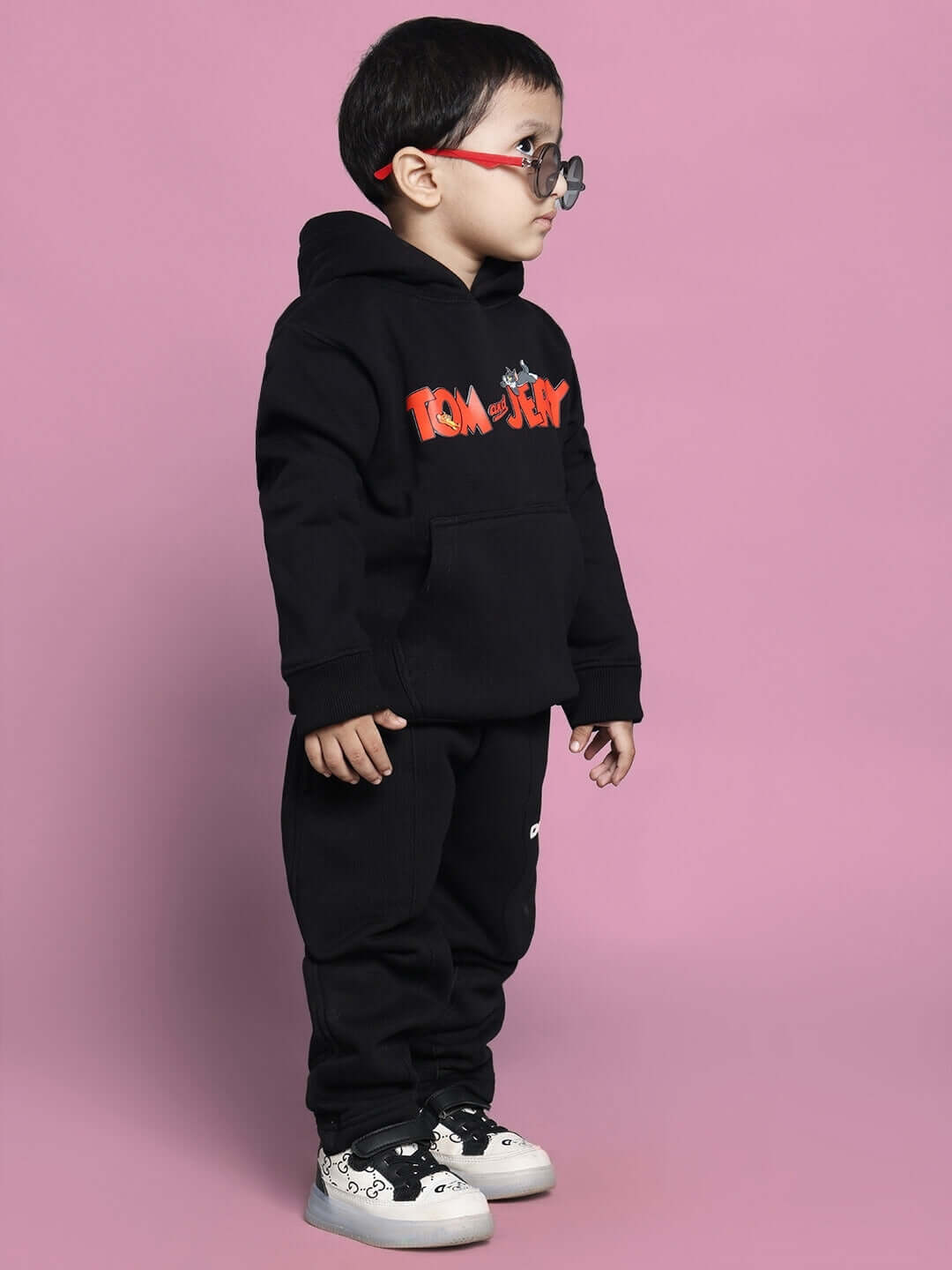 Child wearing Tom & Jerry black co-ord set for boys and girls, featuring a hoodie and pants, against a pink backdrop.