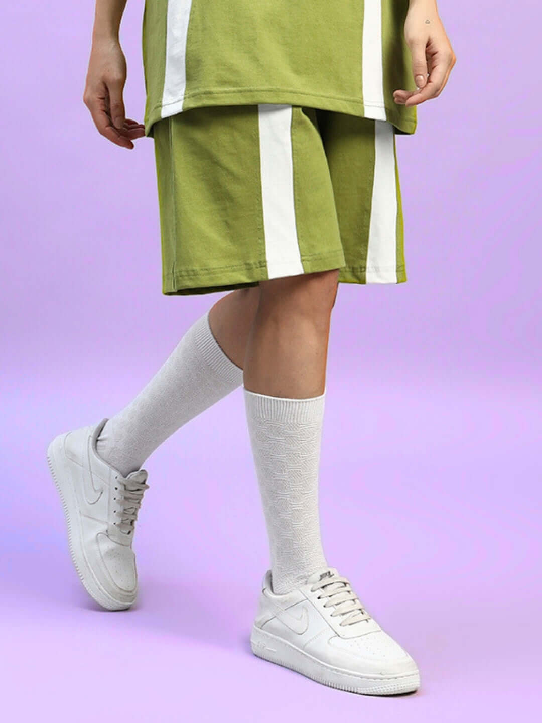 Woman wearing olive green wideline shorts with white accents and sneakers.