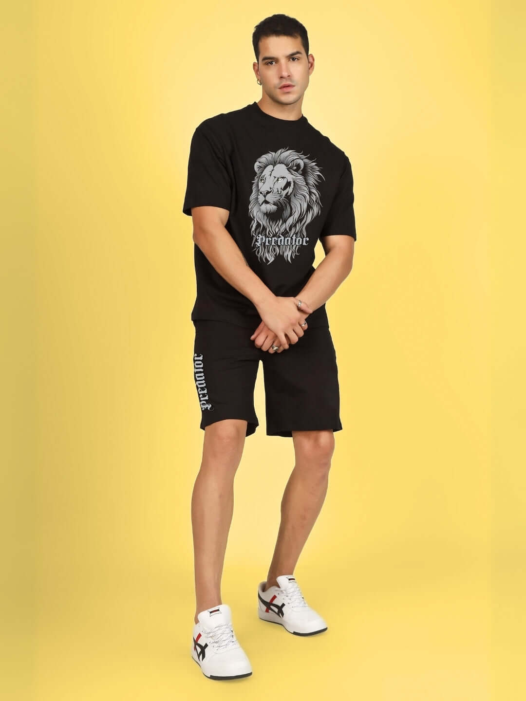 Man wearing black PREDATOR LEGND printed summer co-ord set with a lion graphic, made of cotton French Terry Lycra, against yellow background.