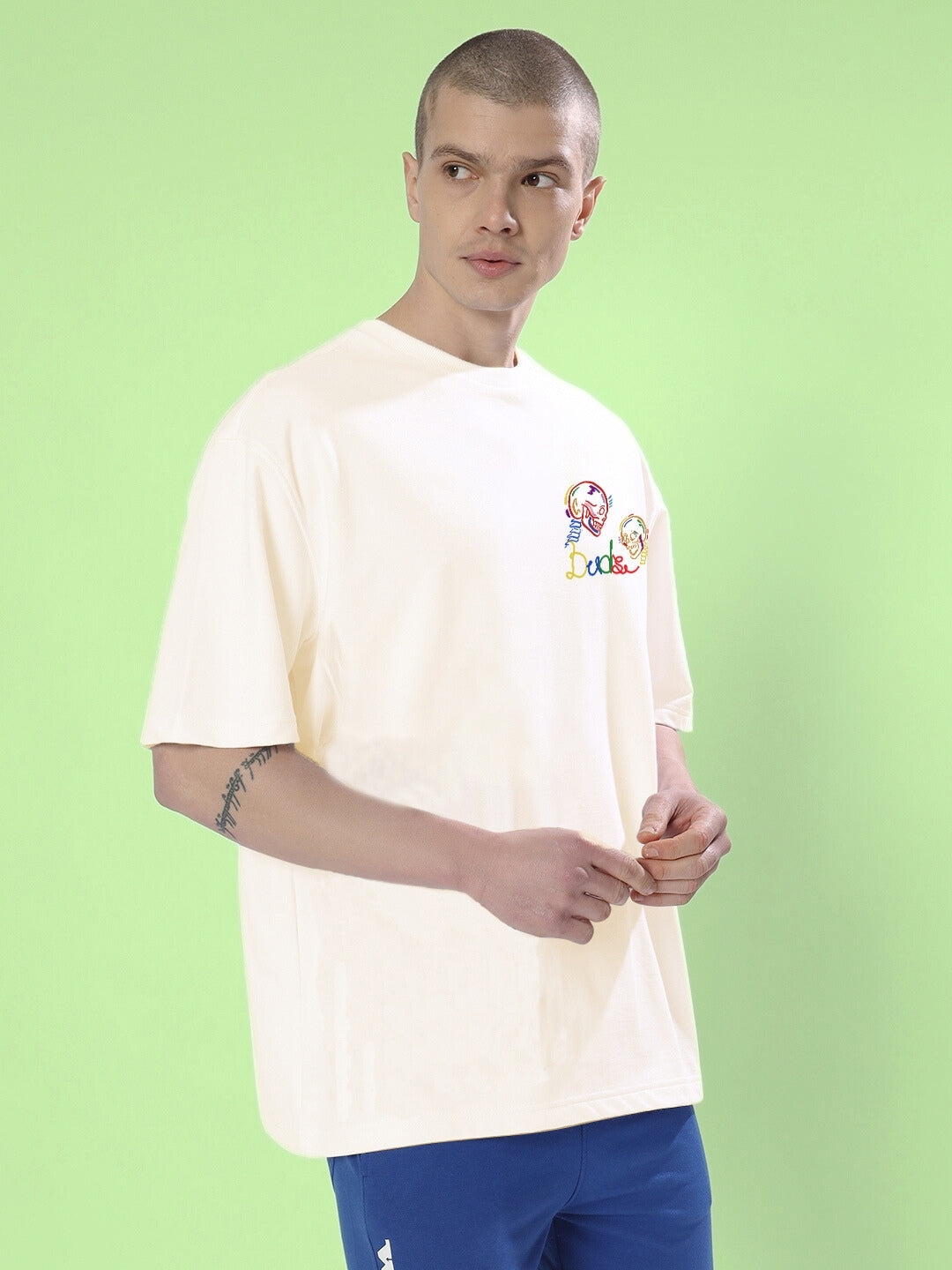 Model wearing SKULL ROLL OVERSIZED T-SHIRT OFF WHITE with skull design, standing against a green background