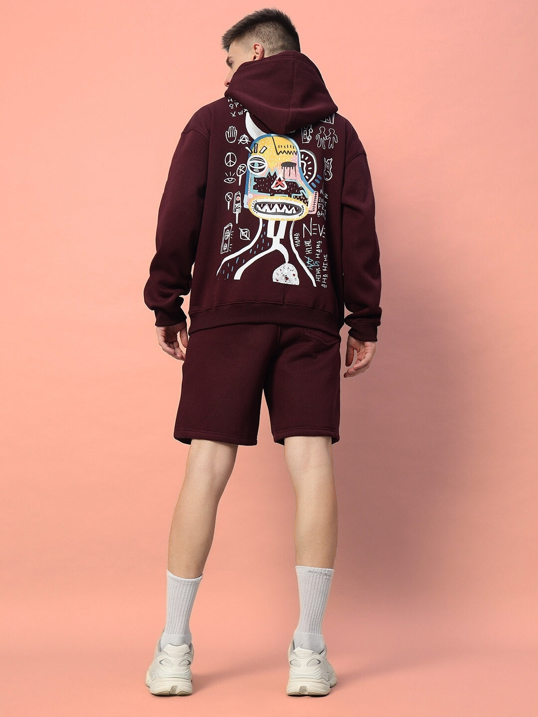 Back view of a wine-colored JUMBLED FLEECE CO-ORD with graphic artwork, featuring shorts and a hoodie on a peach background.