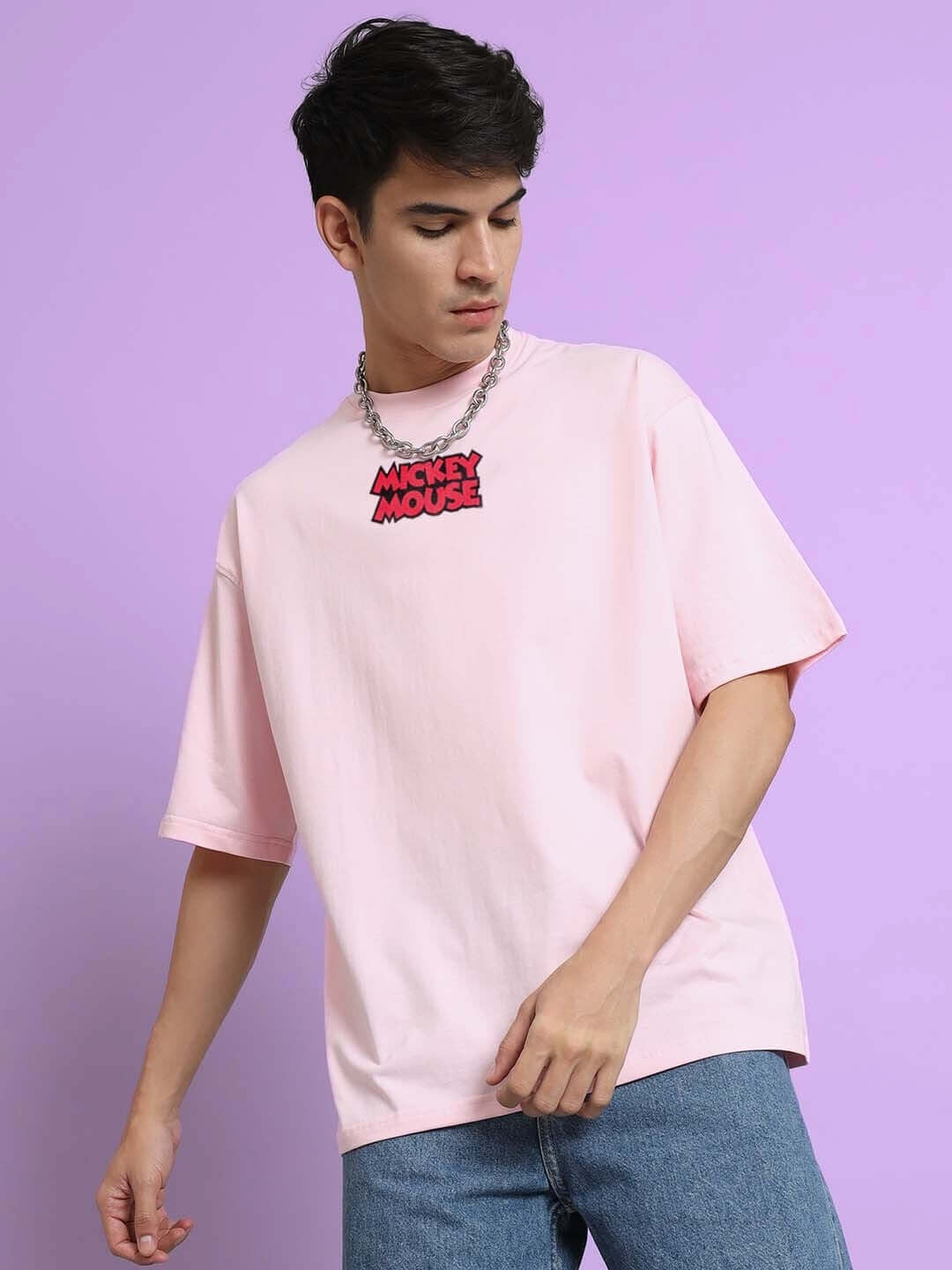 Man wearing DUDS MOUSE OVER-SIZED T-SHIRT PINK with a Mickey Mouse necklace on a purple background.