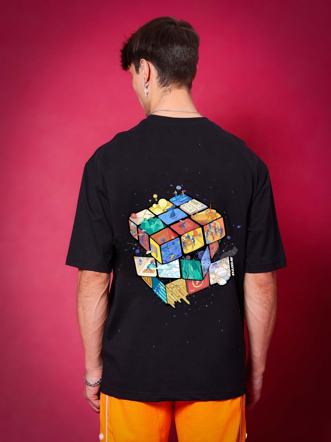 Person wearing RUBIK REVOLUTION OVERSIZED T-SHIRT BLACK with colorful design on back.