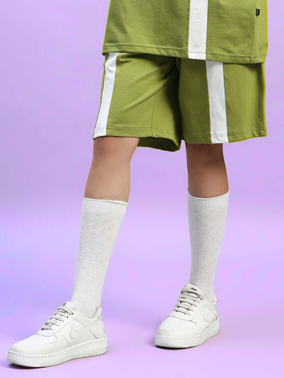 Model wearing Women's Wideline Regular Fit Shorts in olive green with white stripe detail, paired with white socks and sneakers.