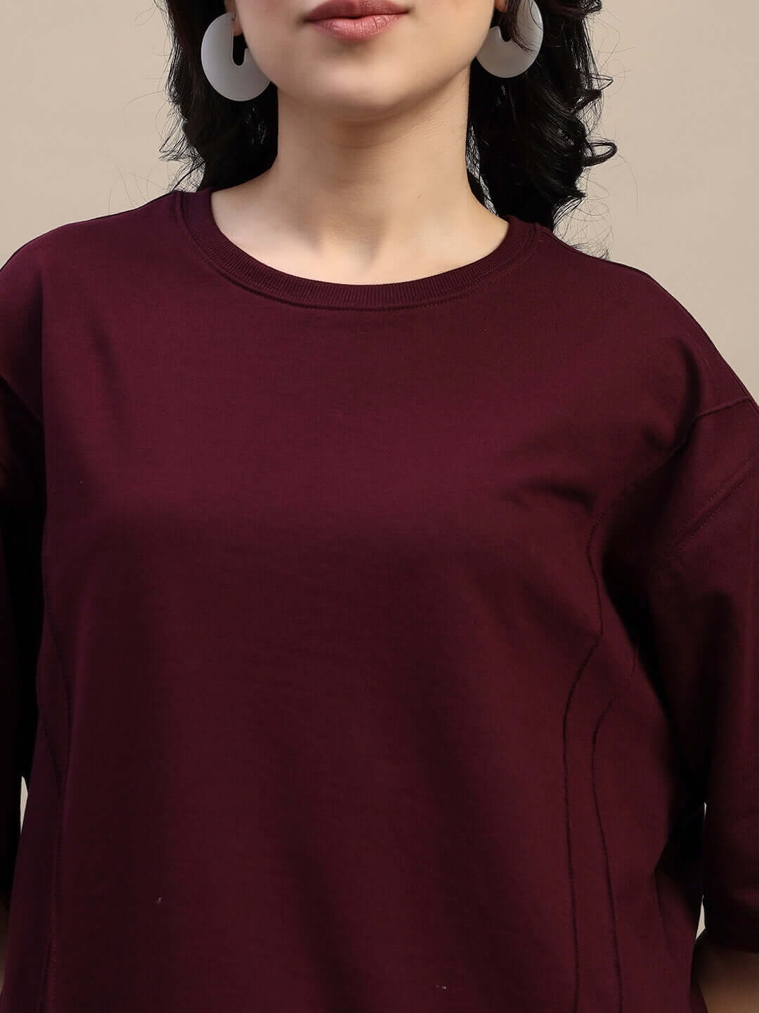 Women's maroon oversized T-shirt, premium cotton, French terry lycra blend, styled with hoop earrings, front view.
