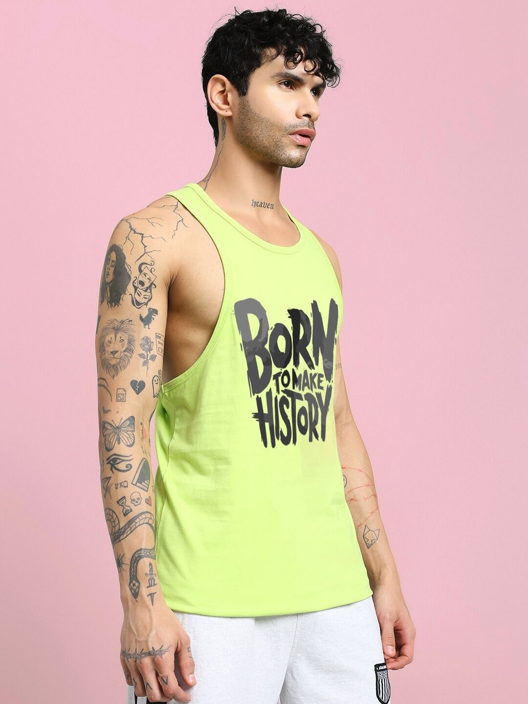 Man wearing BORN TO MAKE HISTORY GYM VEST T-SHIRT NEON GREEN with tattoos on pink background.