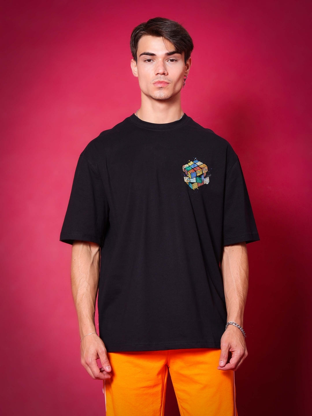 Model wearing RUBIK REVOLUTION OVERSIZED T-SHIRT BLACK with colorful cube design on front, showcasing casual fashion in red background.