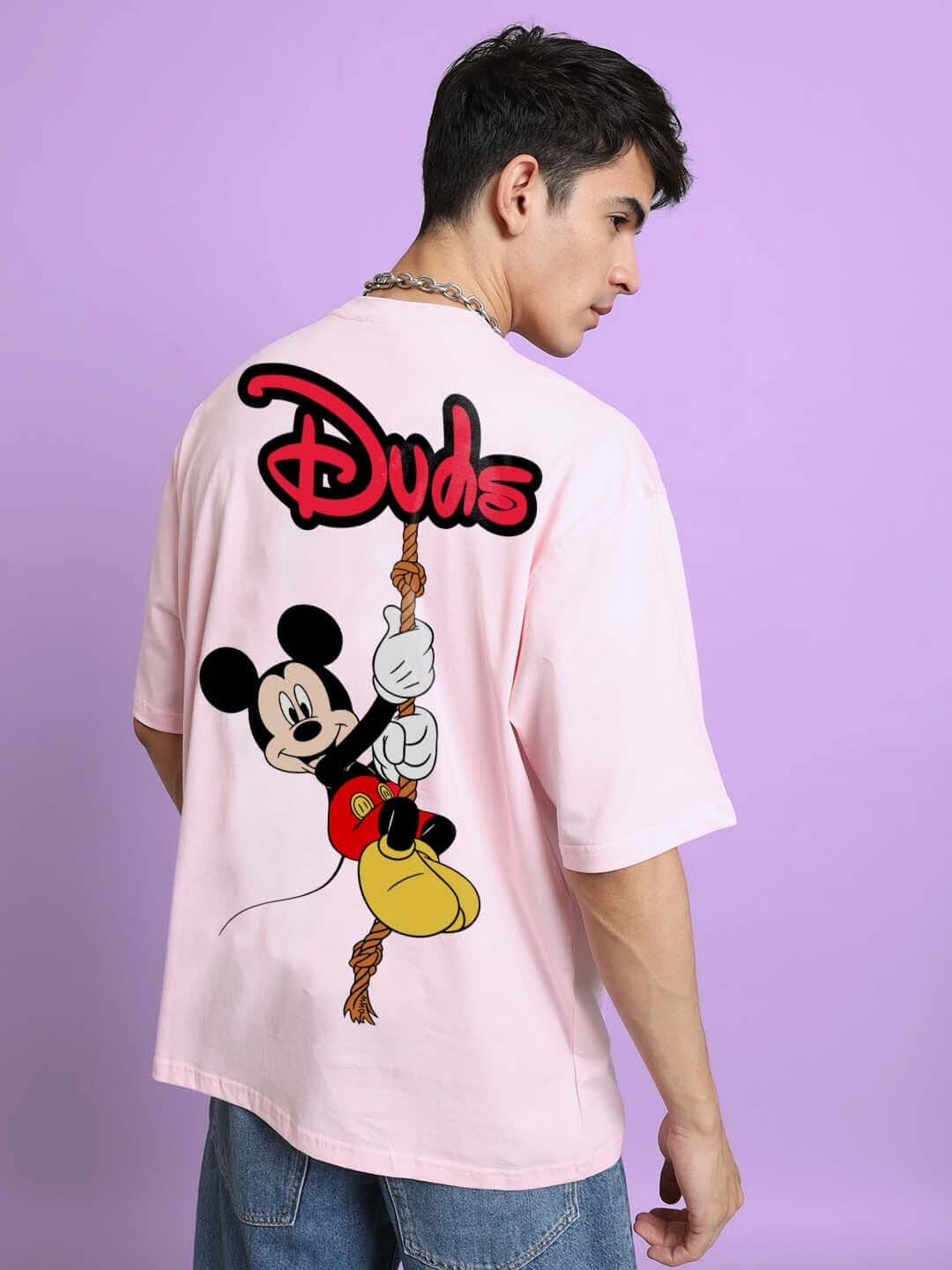 Back view of DUDS MOUSE OVER-SIZED T-SHIRT PINK featuring cartoon character design, worn by a person against a purple background.